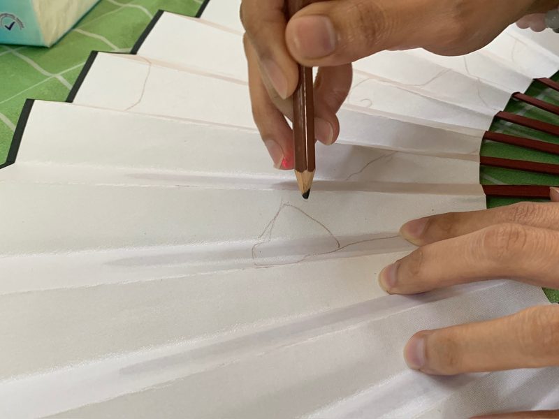 Hand sketching on a blank white fan with a pencil