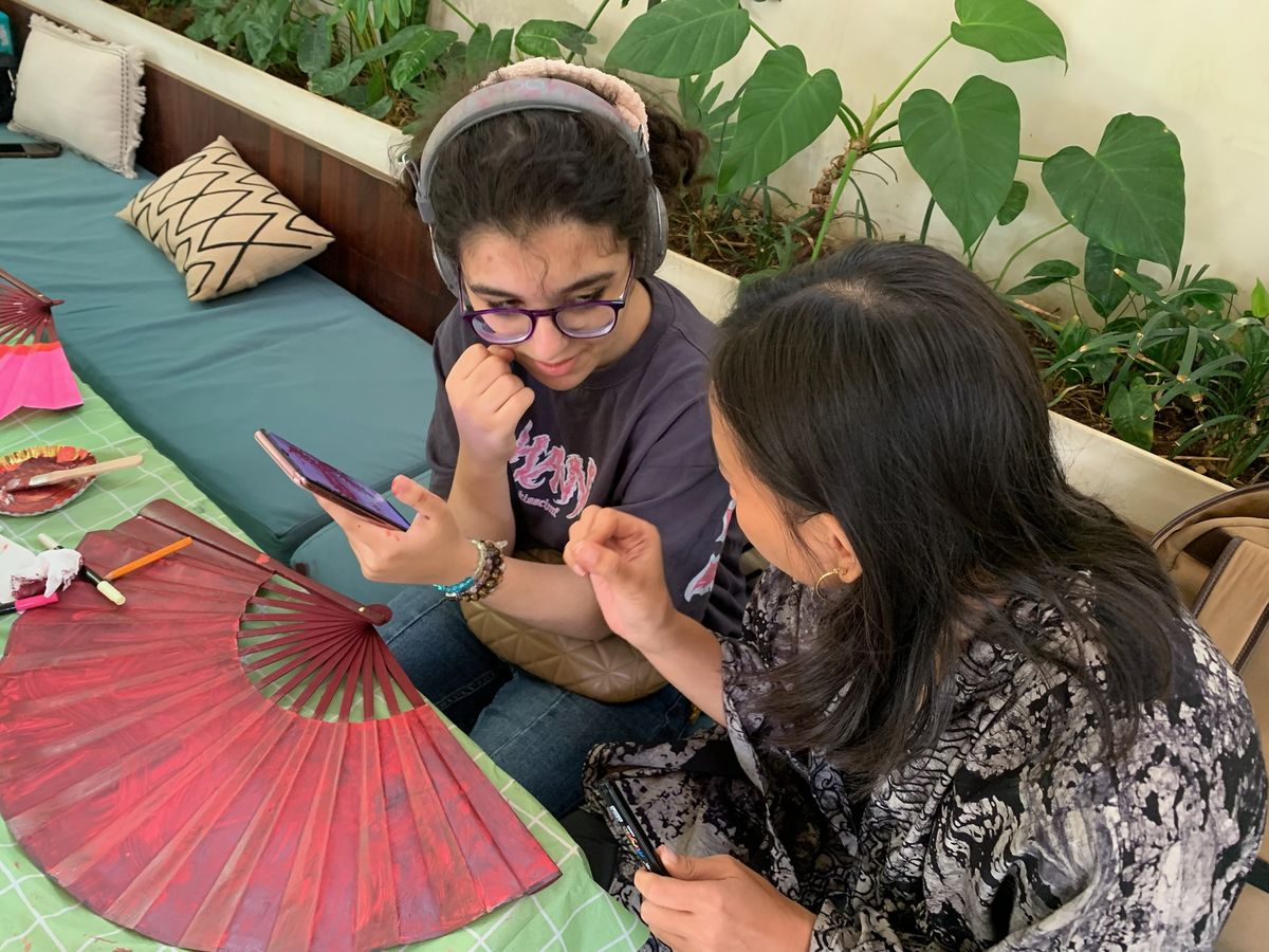Facilitator and a guest choosing a design on a phone, pink fan on the table