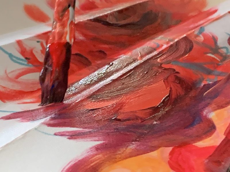 Brush painting red and orange swirls on a fan